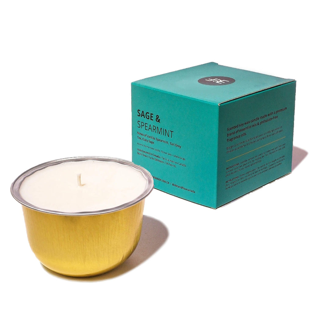 A gold metal candle vessel with white wax sits in front of its teal packaging box on a clean white background. The box is labeled 'SAGE & SPEARMINT' and features a small circular logo at the top.