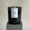 A black glass jar candle with a white label. The label reads 