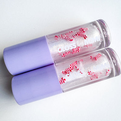 Two lip glosses with purple caps and red and white designs on a light gray background