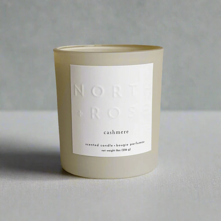 A beige glass jar candle with a white label. The label reads 