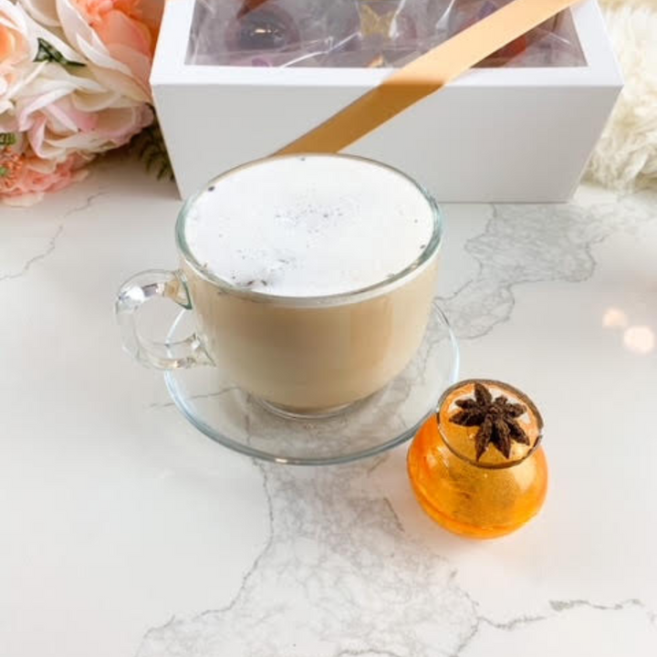 An orange, spherical tea bomb topped with a star anise. The tea bomb is resting on a white marble surface.