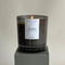 A black glass jar candle with a white label. The label reads 