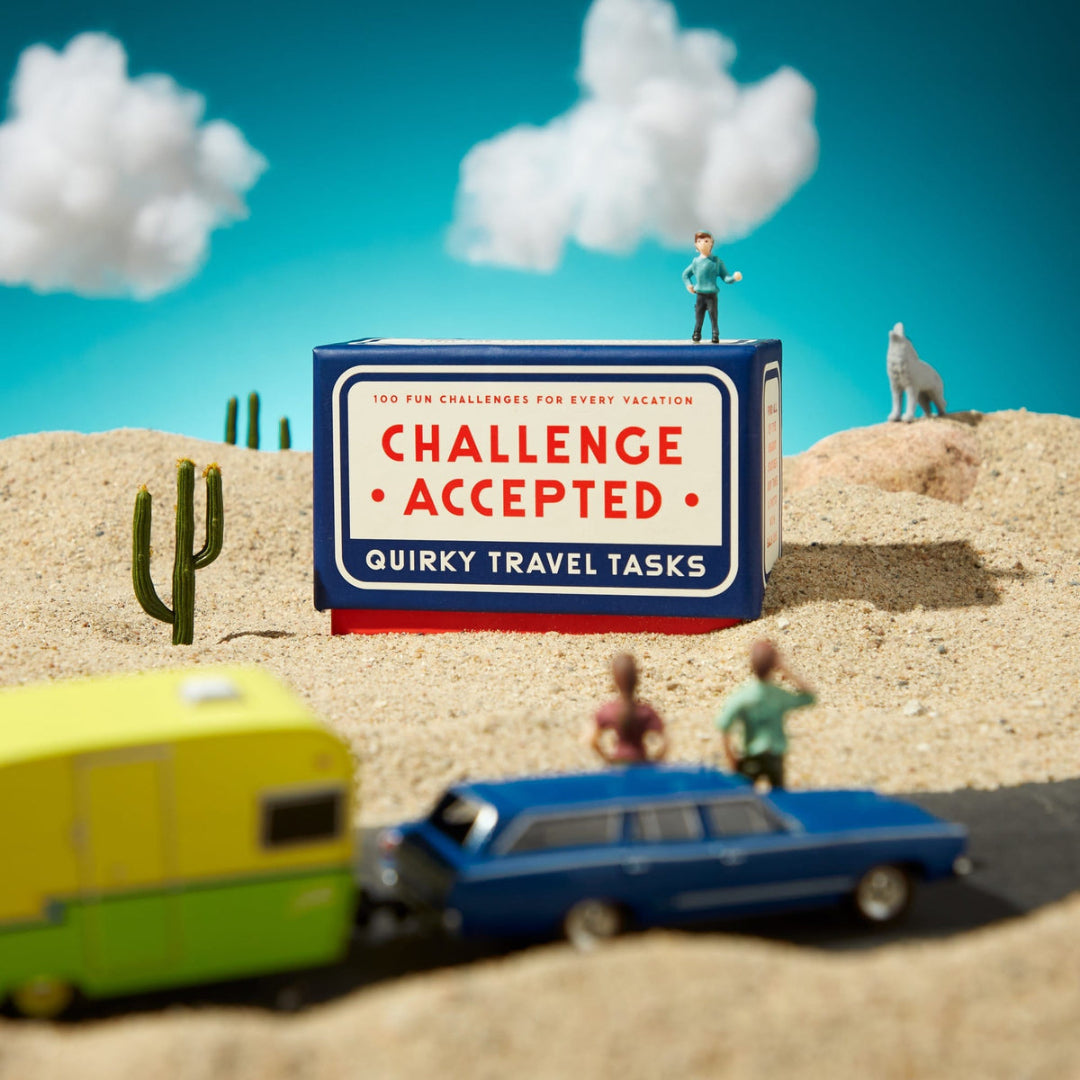 Toy scene with 'Challenge Accepted' box in a desert setting with toy cars and figures.