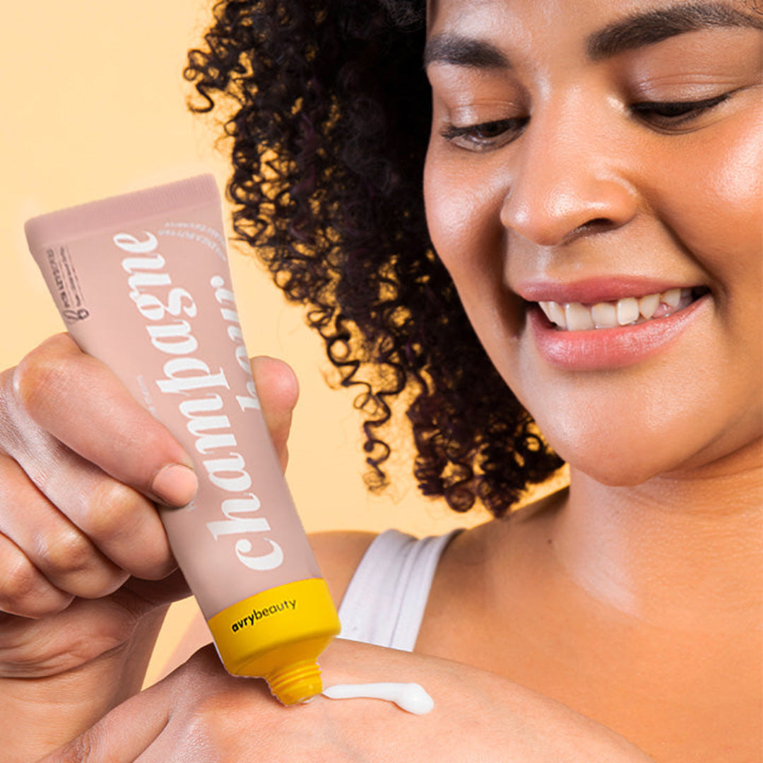 Person applying champagne-colored lotion to their shoulder with a beige background