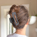 Person with a black hair clip in their hair against a blurred indoor background
