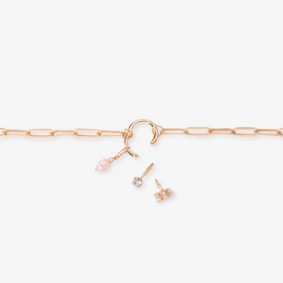 A gold-toned charm necklace with a paper clip link chain, featuring a clasp with attached charms including a white pearl drop and two small crystal pendants, possibly Toniq brand, displayed on a white background. This delicate necklace is available in Ottawa, Ontario, Canada.