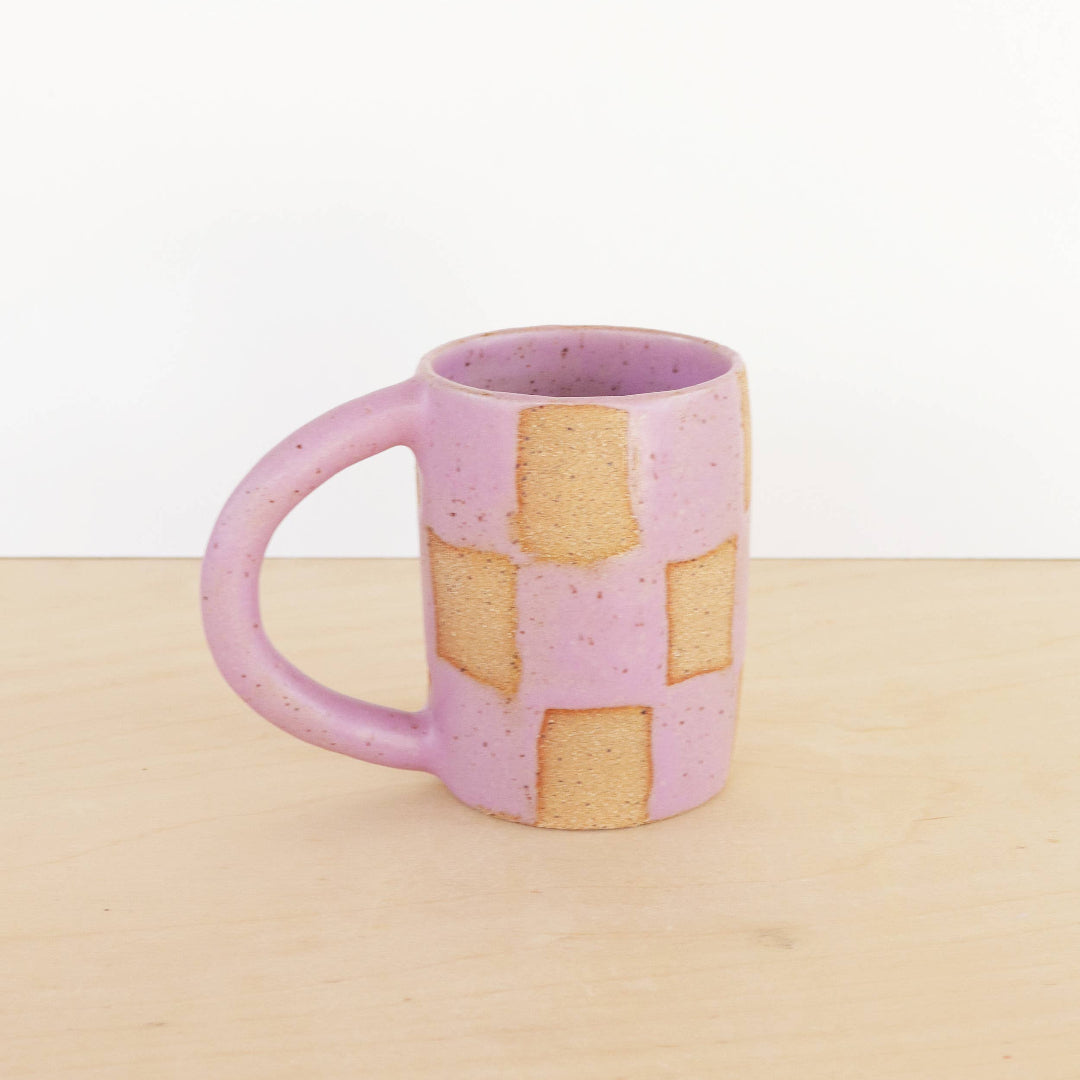 Pink ceramic mug with a checkered pattern on a beige surface