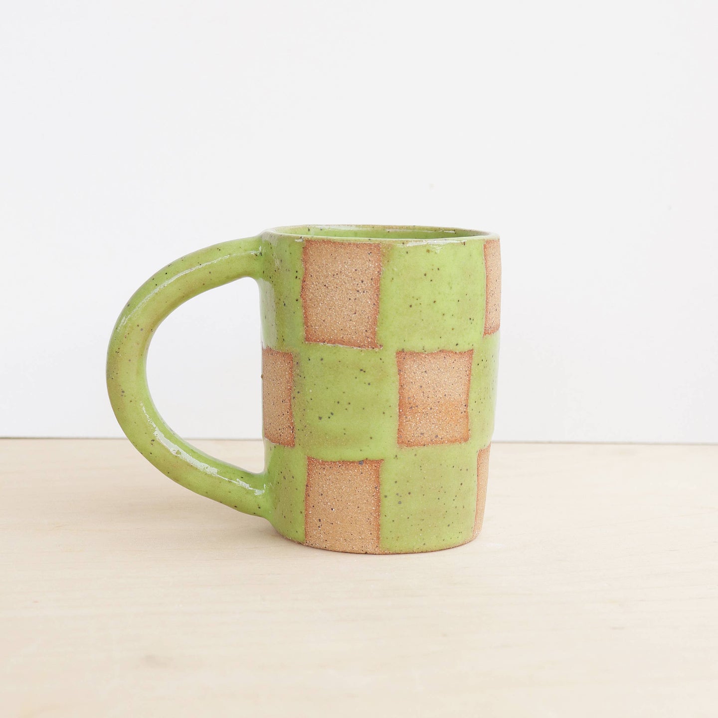 Green ceramic mug with square patterns on a beige surface