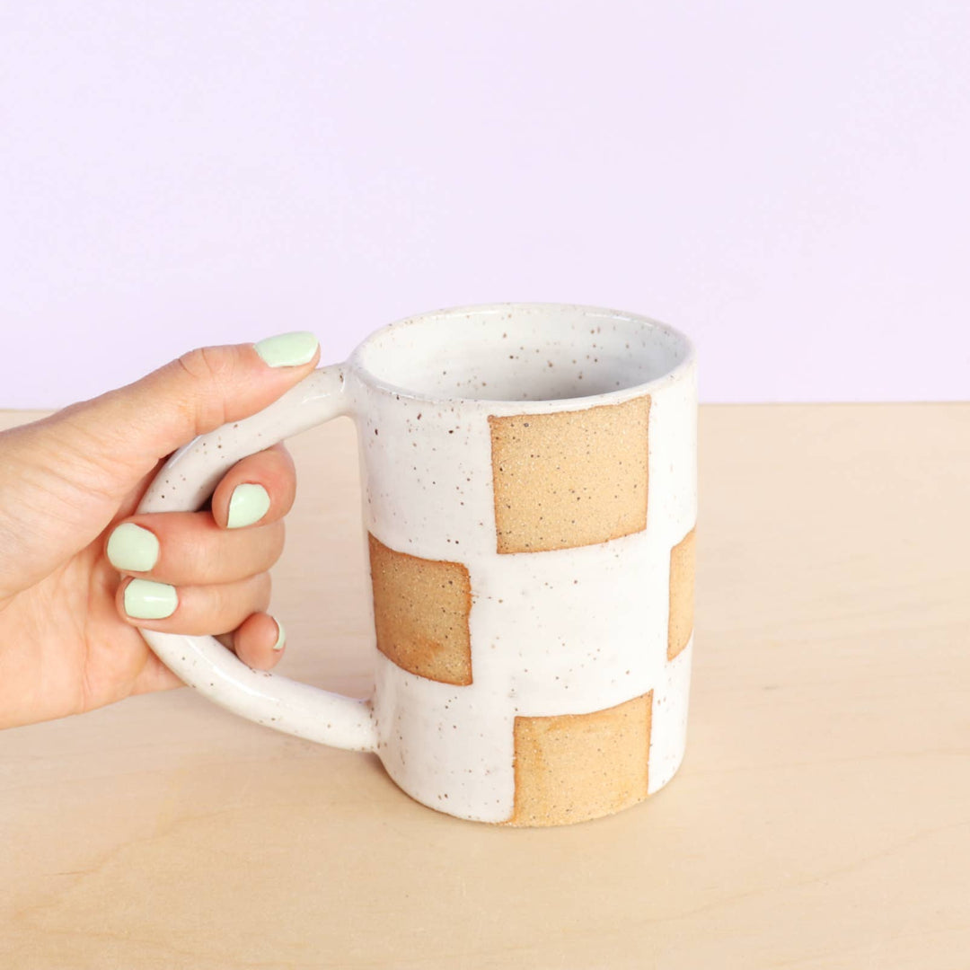Hand holding a ceramic mug with a striped design on a light purple background