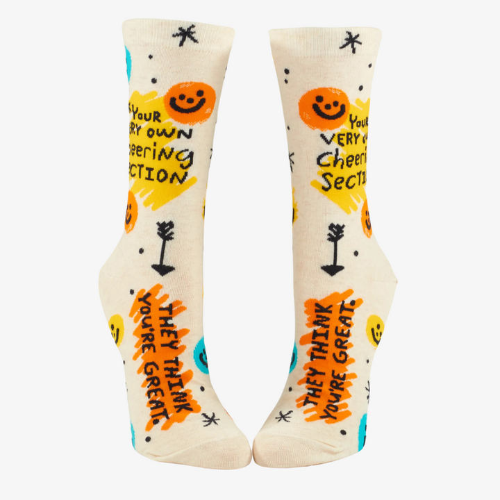 A pair of white crew socks with a fun and colorful design. The socks feature smiley faces, stars, and arrows, along with the text 