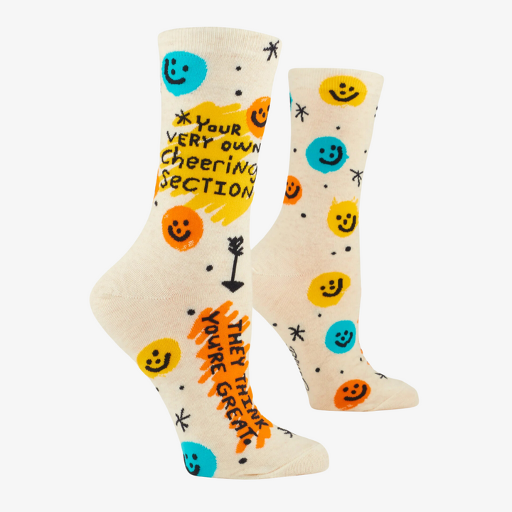 A pair of white crew socks with a fun and colorful design. The socks feature smiley faces, stars, and arrows, along with the text 