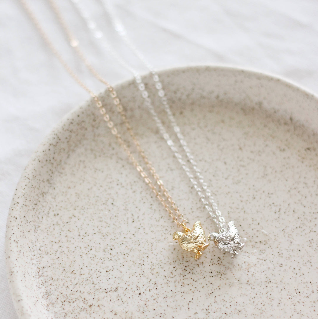 Two necklaces with bird pendants on a speckled ceramic plate.