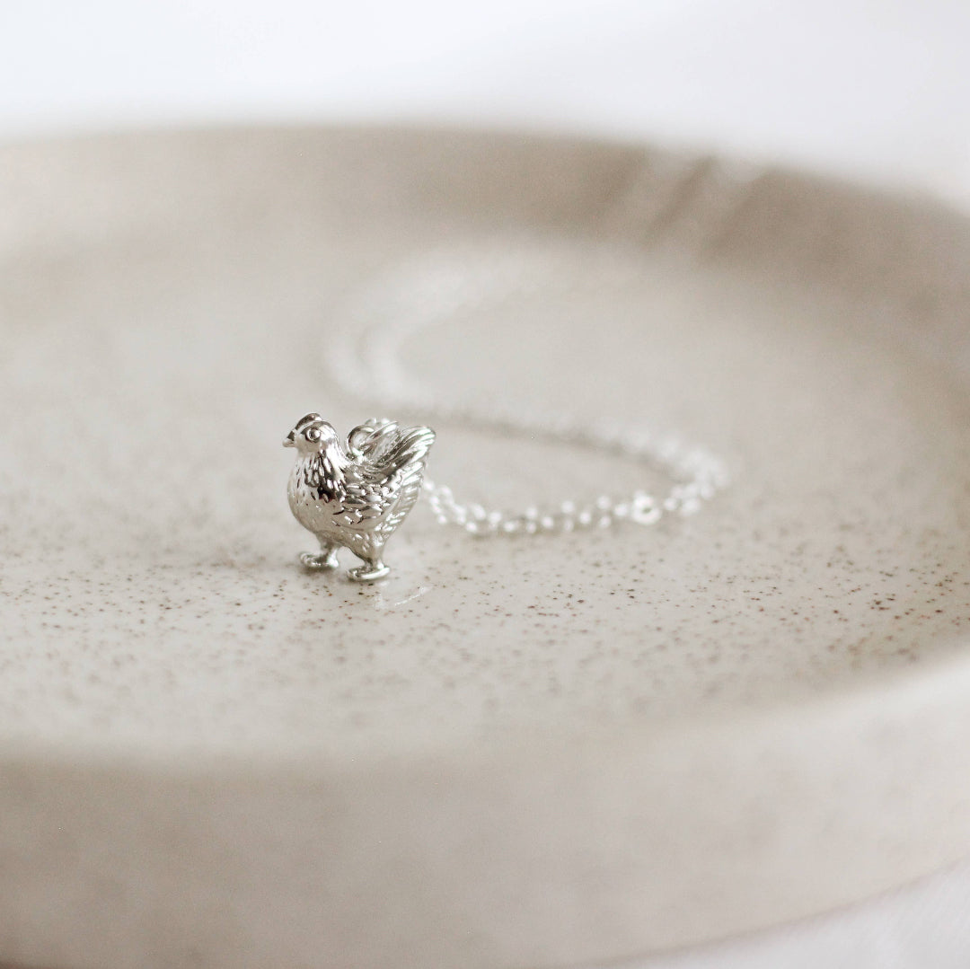 Silver rooster charm on a chain against a white background