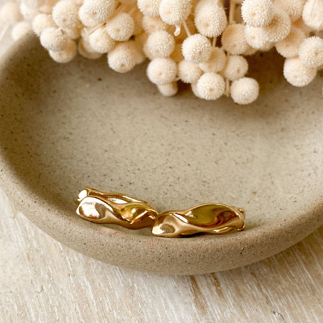 Gold earrings on a beige ceramic dish with decorative white flowers.