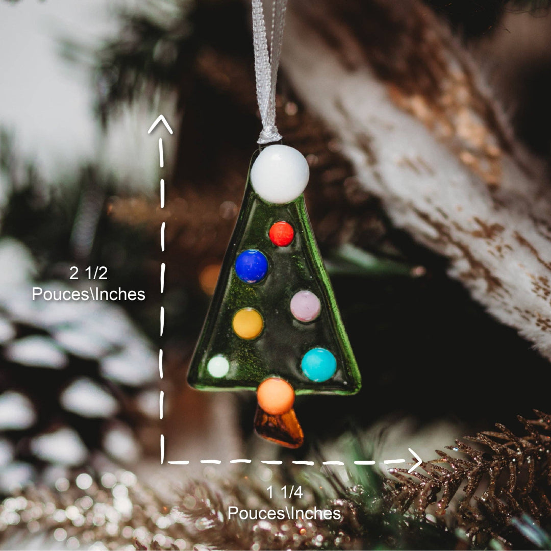 A small Christmas tree ornament made of clear glass with colorful round accents and a white hanging loop, shown hanging in a real environment with pine branches and overlaid dimension labels.