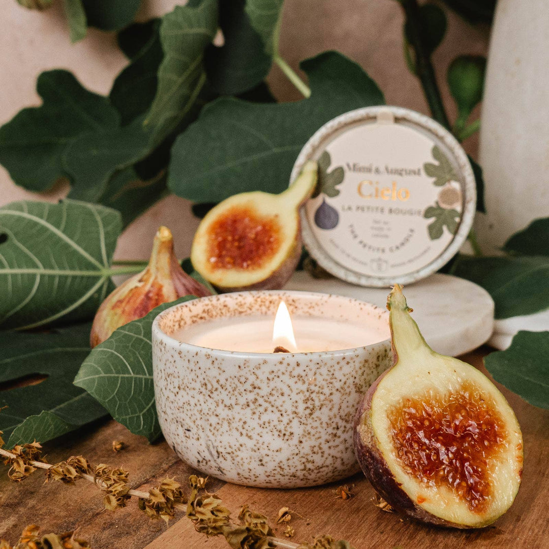 Candle in a speckled container with figs and leaves on a wooden surface