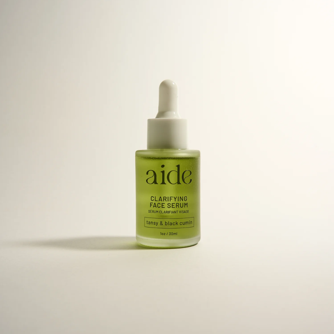 Aide Bodycare Clarifying Face Serum, featuring a small glass bottle with a dropper and a label with 'aide' logo, 'Clarifying Face Serum', and 'tansy & black cumin' text, displayed on a light-colored surface with a soft shadow. The serum is natural and available in Ottawa, Ontario, Canada.
