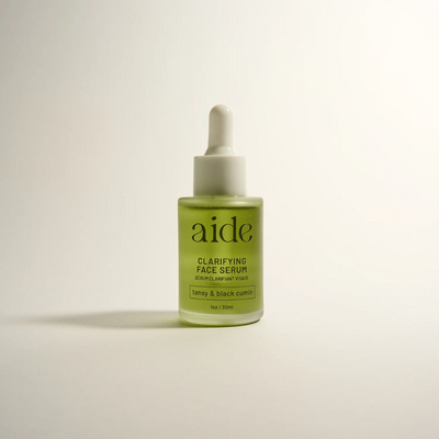 Aide Bodycare Clarifying Face Serum, featuring a small glass bottle with a dropper and a label with 'aide' logo, 'Clarifying Face Serum', and 'tansy & black cumin' text, displayed on a light-colored surface with a soft shadow. The serum is natural and available in Ottawa, Ontario, Canada.