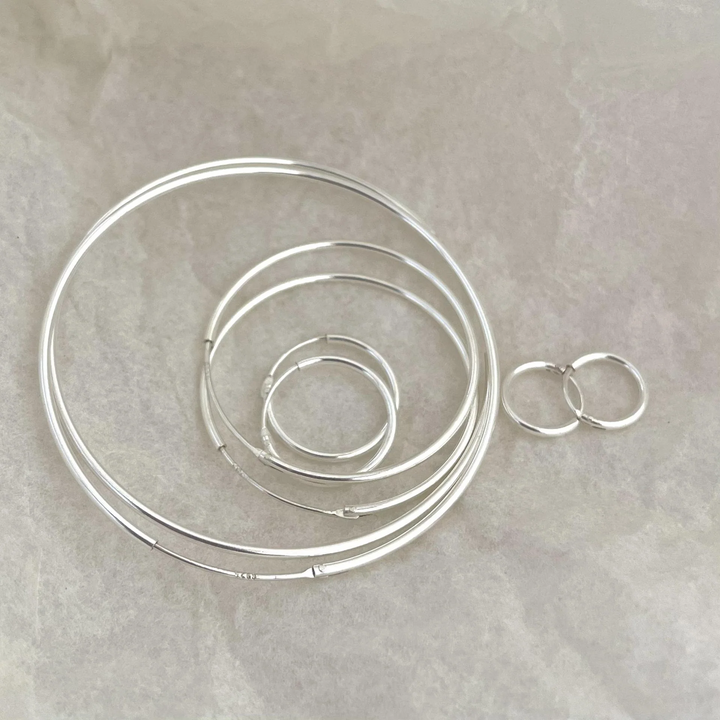 A set of classic hoop earrings made of 925 sterling silver, featuring various sizes of thin, polished silver hoops, displayed on a brown and textured surface. These simple and elegant earrings are available in Ottawa, Ontario, Canada.
