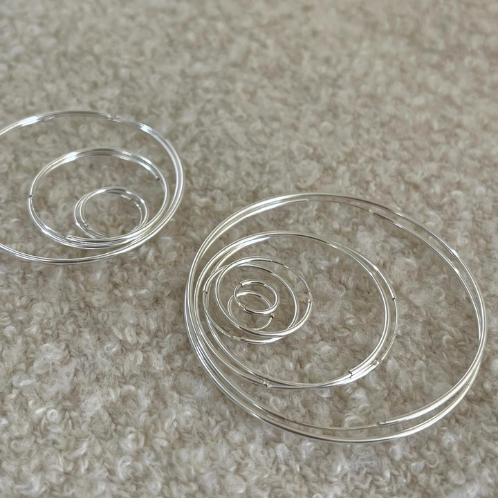 A set of classic hoop earrings made of 925 sterling silver, featuring various sizes of thin, polished silver hoops, displayed on a brown and textured surface. These simple and elegant earrings are available in Ottawa, Ontario, Canada.