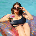 Woman in a black swimsuit holding a cocktail on a glittery inflatable ring in a pool.