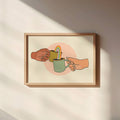 Framed artwork of two hands sharing a cup with a straw on a beige wall.