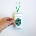 Small plush toy resembling a coffee cup with a green logo held by a hand on a white background