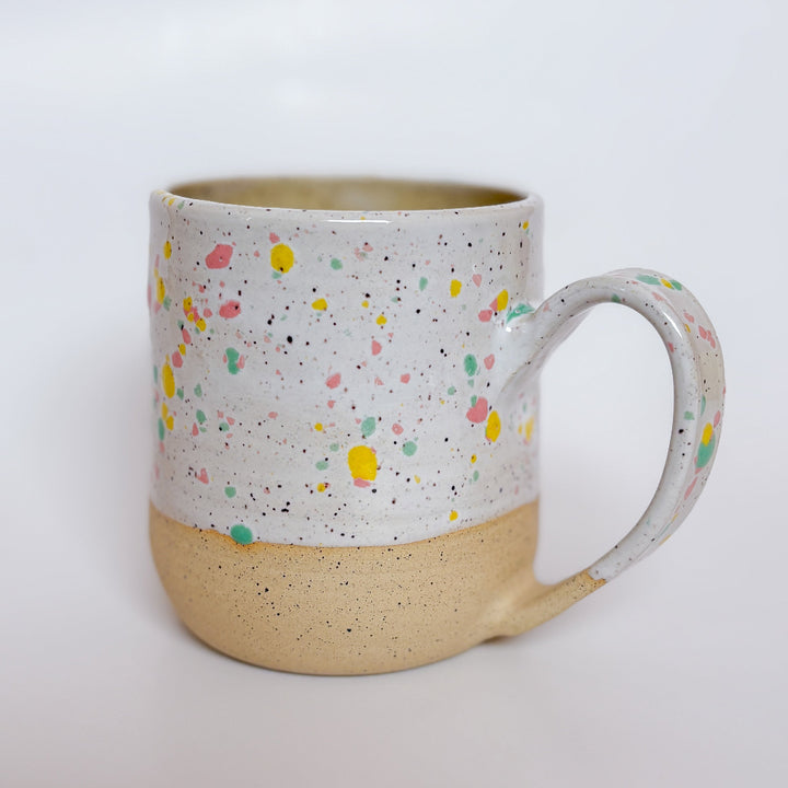 A handmade ceramic mug by Valerie Daoust Ceramics, featuring a white glaze with colorful speckles (pink, yellow, green), displayed on a light gray background. The mug has a large, rounded handle, a speckled texture, and is made in Mississippi Mills, Ontario, Canada.