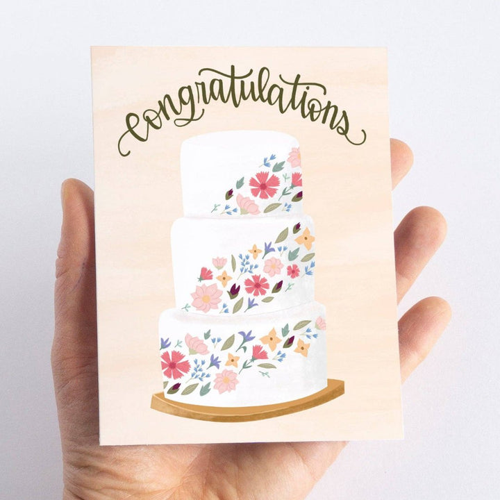 A congratulations card featuring a three-tiered wedding cake decorated with colorful flowers. The word 