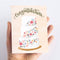 A congratulations card featuring a three-tiered wedding cake decorated with colorful flowers. The word 