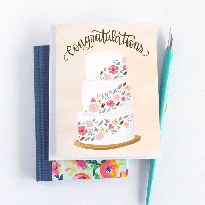 A congratulations card featuring a three-tiered wedding cake decorated with colorful flowers. The word 