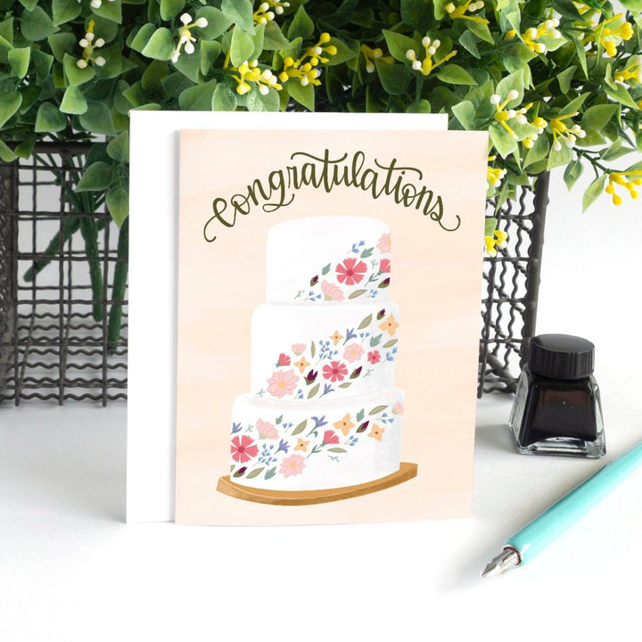 A congratulations card featuring a three-tiered wedding cake decorated with colorful flowers. The word 