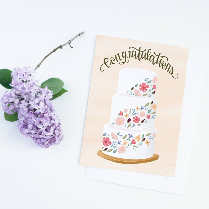 A congratulations card featuring a three-tiered wedding cake decorated with colorful flowers. The word 