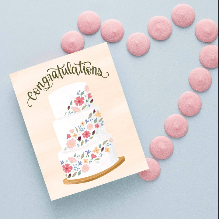 A congratulations card featuring a three-tiered wedding cake decorated with colorful flowers. The word 