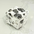 A square marshmallow with swirls of white and black Oreo cookie pieces. The marshmallow is resting on a white marble surface.