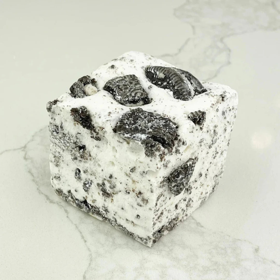 A square marshmallow with swirls of white and black Oreo cookie pieces. The marshmallow is resting on a white marble surface.