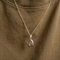 A copper oval locket necklace with an engraved evil eye design, featuring an eye with radiating lines and crescent moons, hanging from a gold chain. This is a protective and spiritual piece of jewelry, available in Ottawa, Ontario, Canada.
