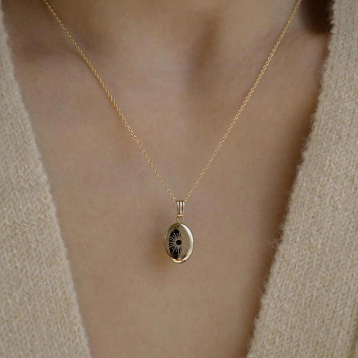A copper oval locket necklace with an engraved sun design, featuring radiating lines, worn by a person against a light-colored sweater. This is a celestial and radiant piece of jewelry, available in Ottawa, Ontario, Canada.