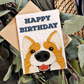 Birthday card with a corgi illustration and 'Happy Birthday' text, surrounded by leaves.