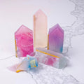 A group of crystal-shaped candies in various pastel colors, including pink, purple, and white. Some of the candies have gold accents. The candies are arranged on a white marble surface.