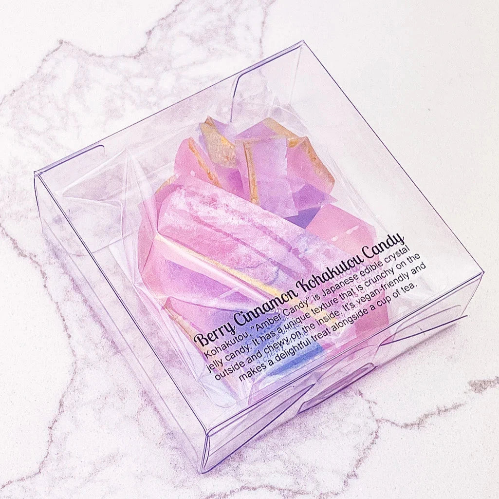 A group of crystal-shaped candies in various pastel colors, including pink, purple, and white. Some of the candies have gold accents. The candies are arranged on a white marble surface.