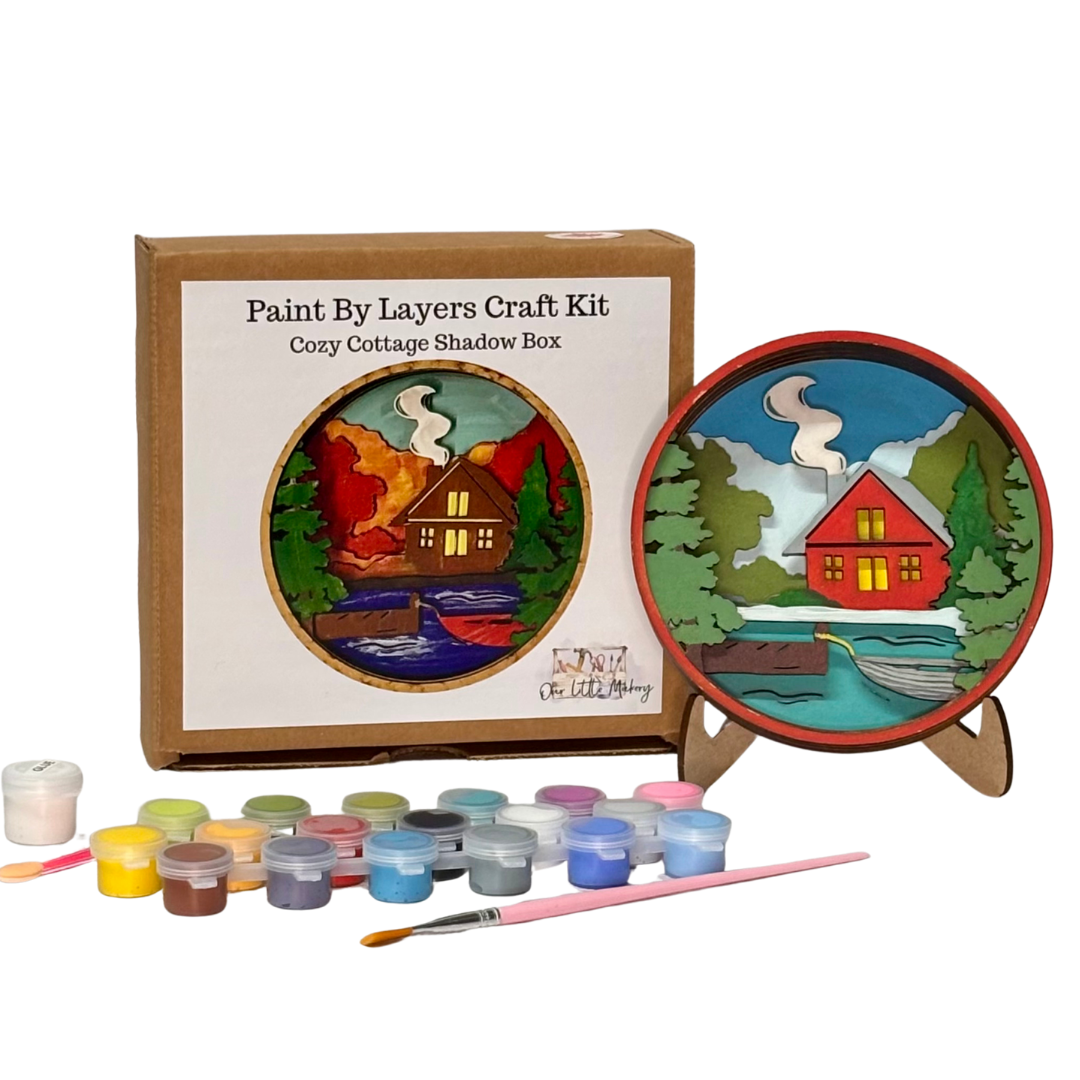 Paint by layers craft kit with a completed shadow box painting of a cottage scene.
