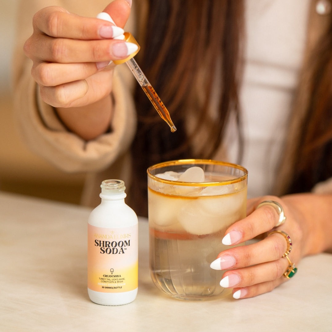 Person adding a dropper of liquid to a glass of Shroom Soda.