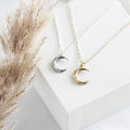 Two moon-shaped pendants on necklaces with a neutral background