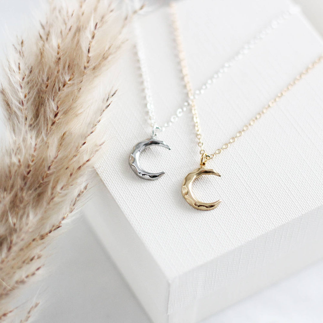 Two moon-shaped pendants on necklaces with a neutral background