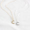 Two crescent moon necklaces on a white cloth. One necklace has a gold-colored crescent moon pendant, and the other has a silver-colored crescent moon pendant. Both necklaces have delicate chains.