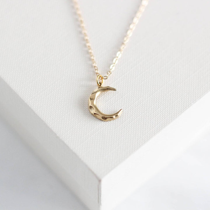 a gold-colored crescent moon pendant on a delicate gold chain.
