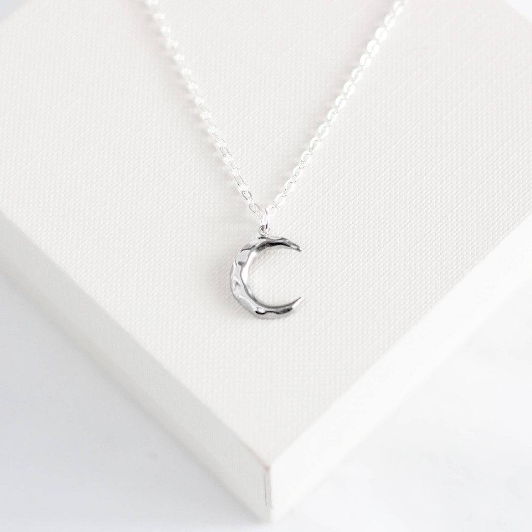 Silver necklace with a crescent moon pendant on a white background