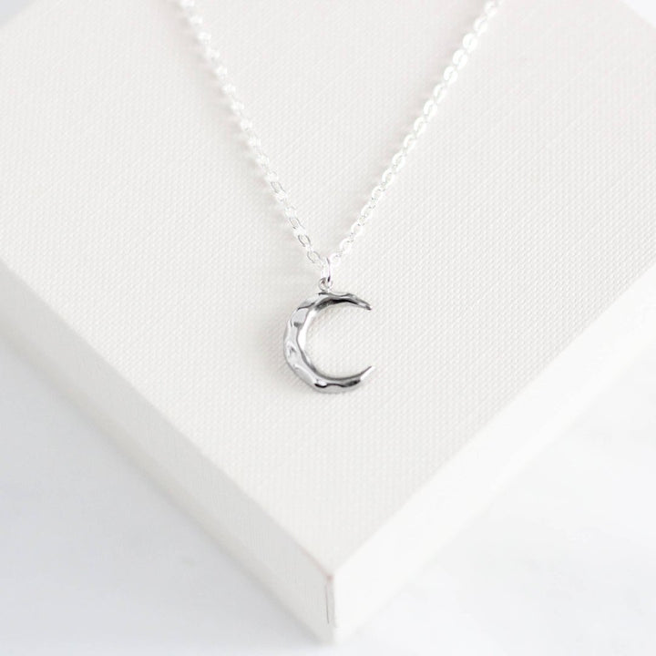 a silver-colored crescent moon pendant on a delicate silver chain.