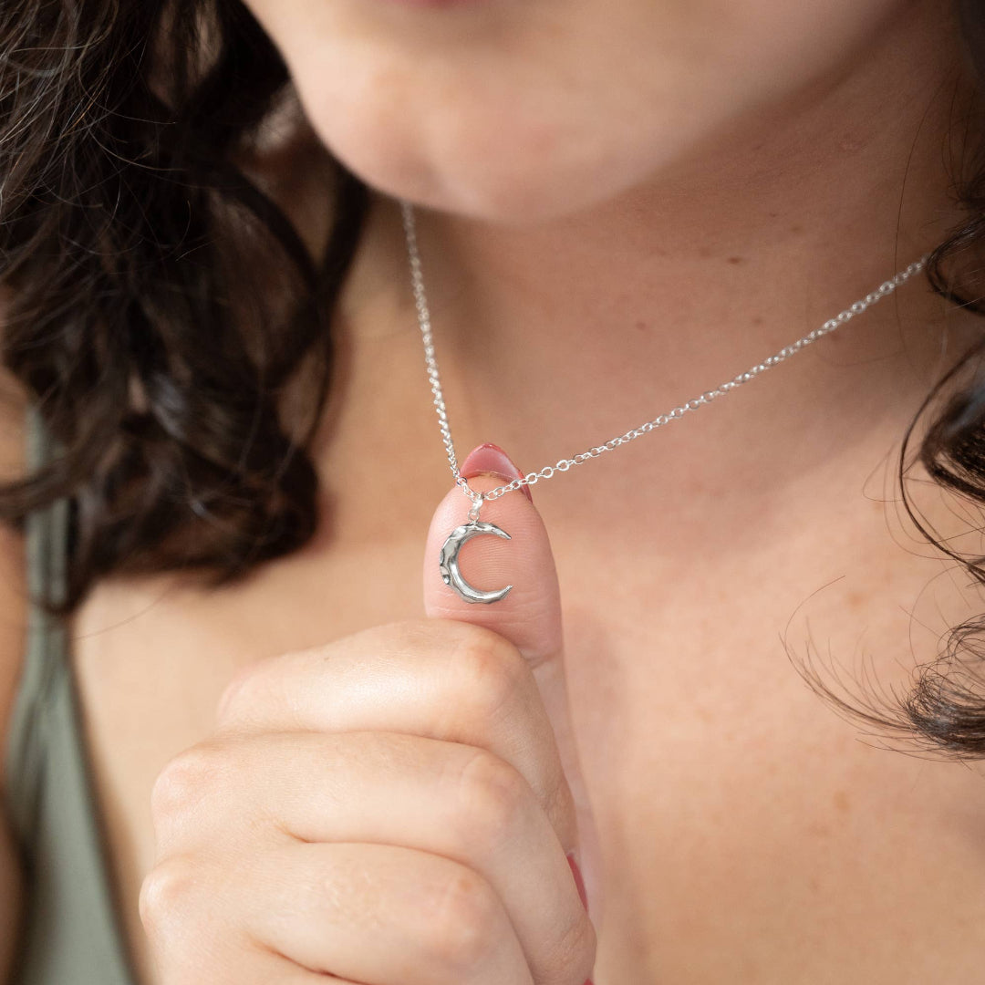 Close-up of a person wearing a silver necklace with a crescent moon pendant.